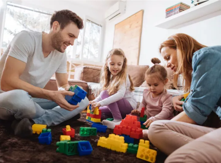 Une famille de quatre personnes assises par terre, jouant ensemble avec des blocs de construction colorés.